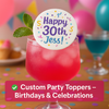 Bright pink cocktail with a custom edible drink topper reading “Happy 30th, Jess!” surrounded by colorful balloons, confetti, and additional drinks, creating a festive birthday party atmosphere.