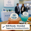 Branded cocktails with custom edible drink toppers featuring the Pulse Tech logo, displayed at a modern trade show booth with a blue and white color scheme, as business professionals engage in conversation in the background.