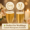 Two champagne flutes with personalized edible drink toppers, featuring gold monogram designs, displayed on an elegant wedding table with soft florals, candles, and warm fairy lights in the background.
