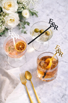 Three cocktails with decorative sticks featuring 'E&J' on a marble surface with flowers and cutlery.