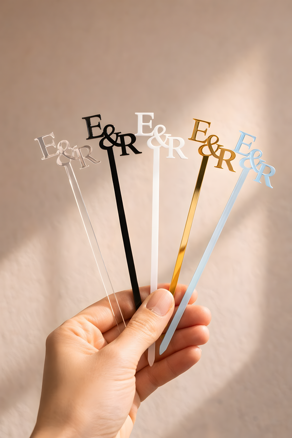 Set of E&R branded stir sticks held by a hand against a neutral background